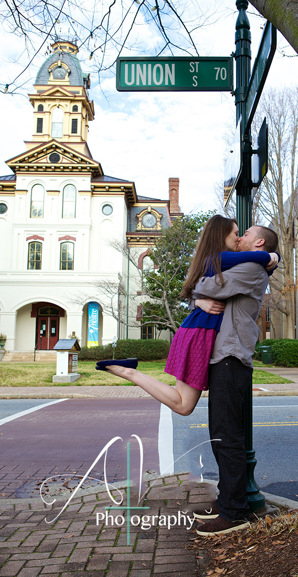 Couple embrace each other and kiss under the UNION St. sign during their Downtown Concord Engagement Session