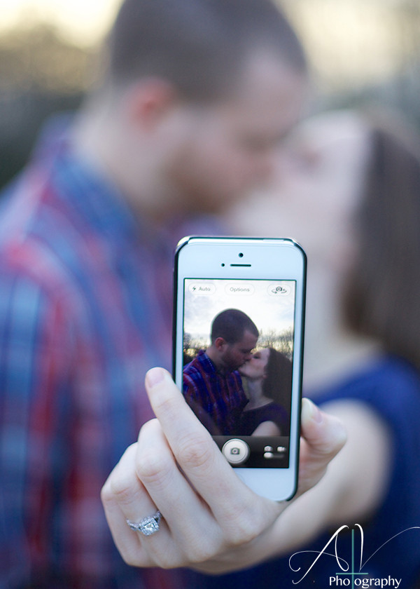 An artistic intimate kiss of a couple on a cell phone showing off the engagement ring during their Downtown Concord Engagement Session
