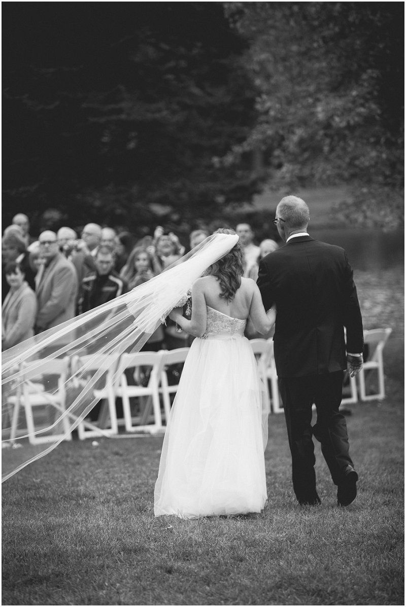 The veil blowing as the brides father walks her down the aisle at the Waterfront wedding at the chetola resort and spa in Blowing rock North Carolina