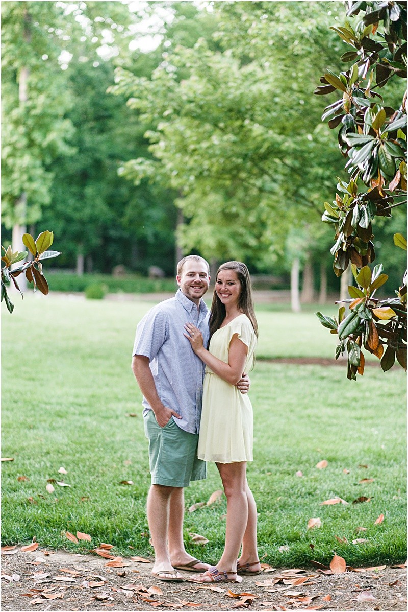between the trees during the engagement session at burr mill park and the greensboro bicentennial gardens