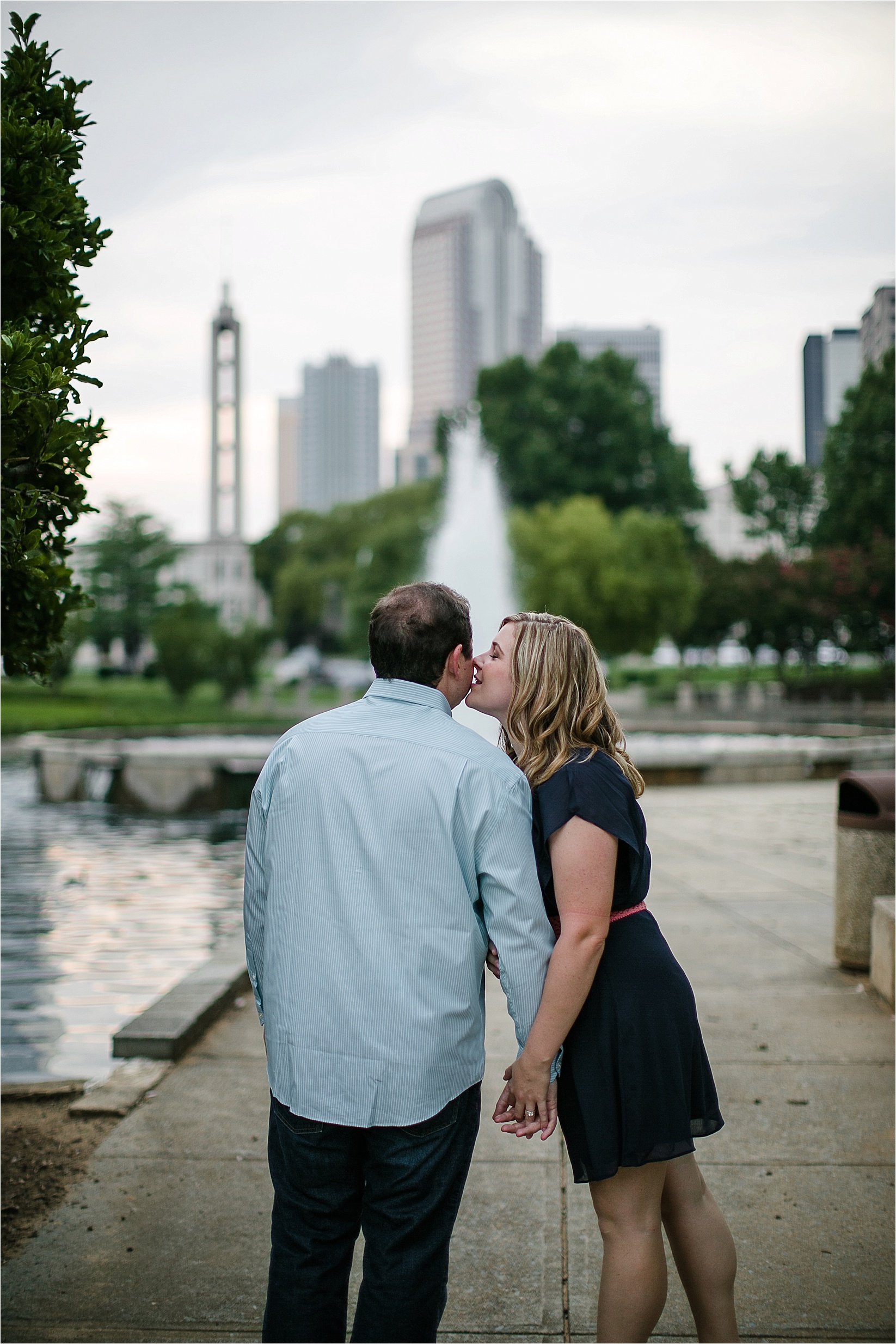 kissing on the cheek with the charlotte skyline at Catherine & Jordan's engagement session at freedom park and marshall park in Charlotte North Carolina