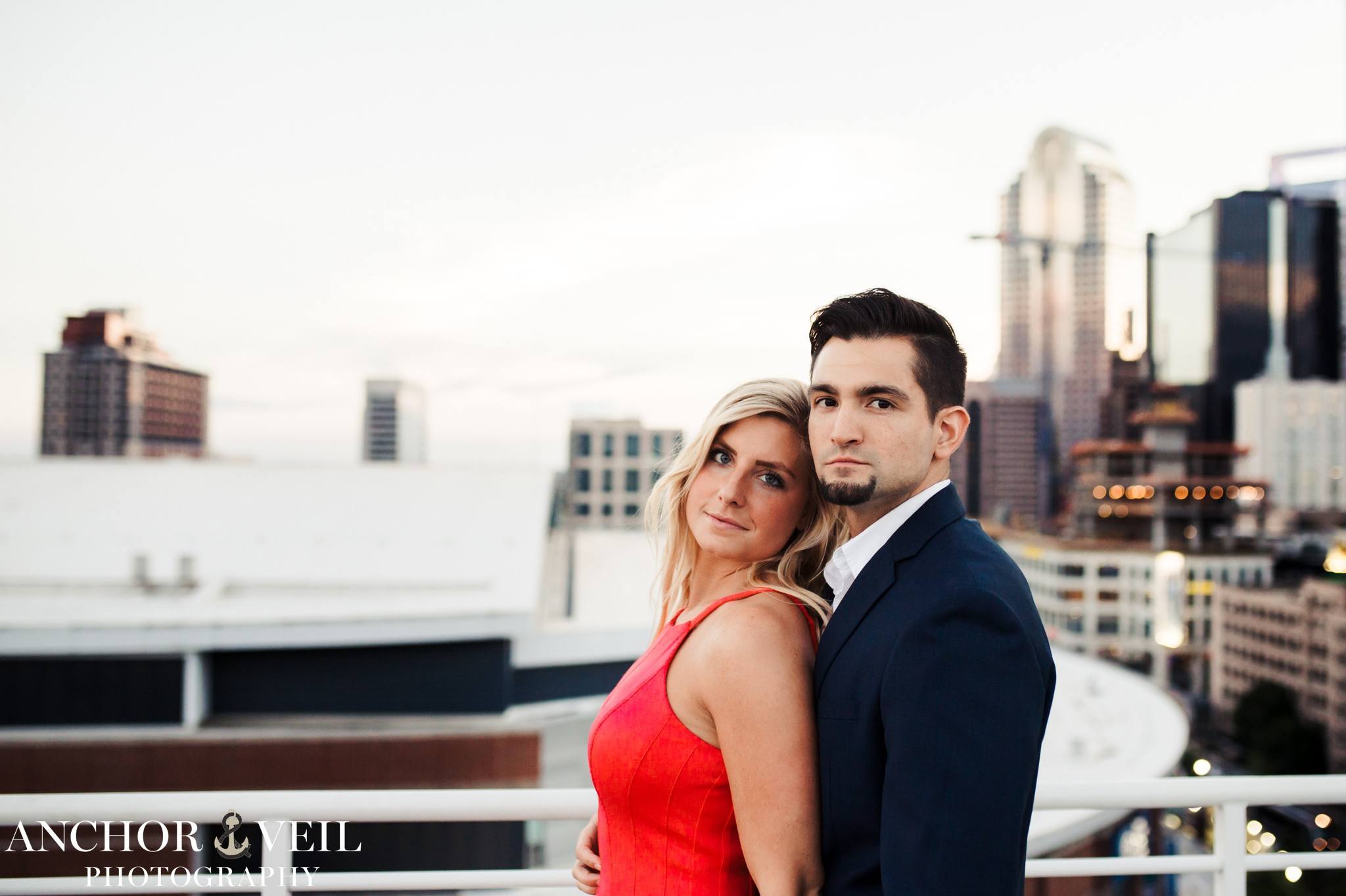 leaning into each other with the charlotte skyline in the background with a red dress.