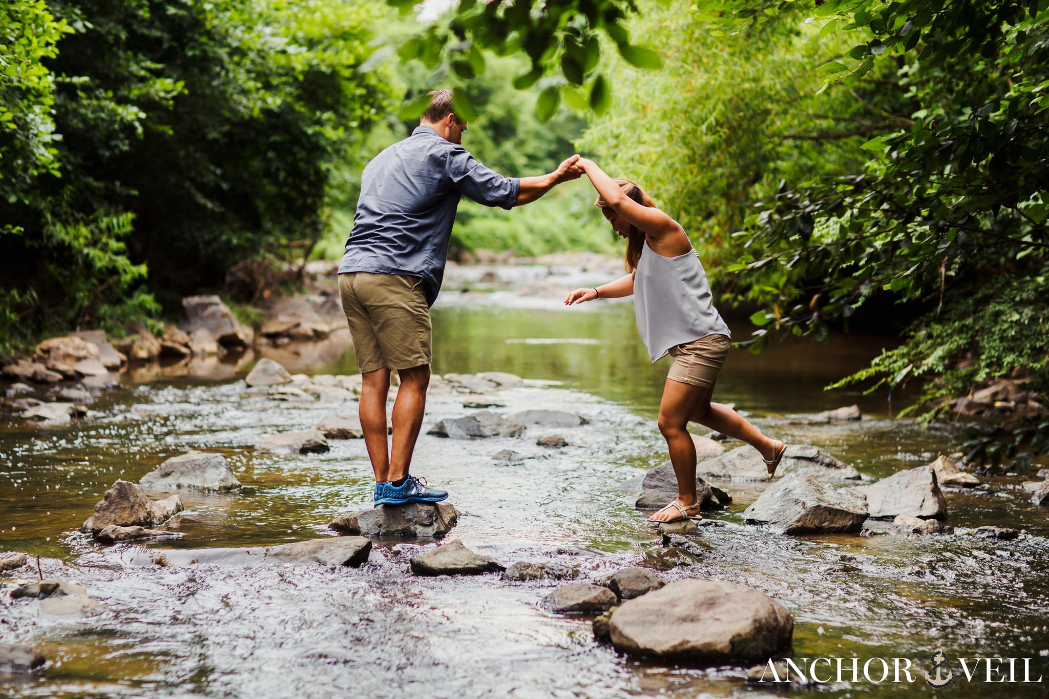 helping her onto the rock while crossing a creek during their Freedom Park Engagement Session