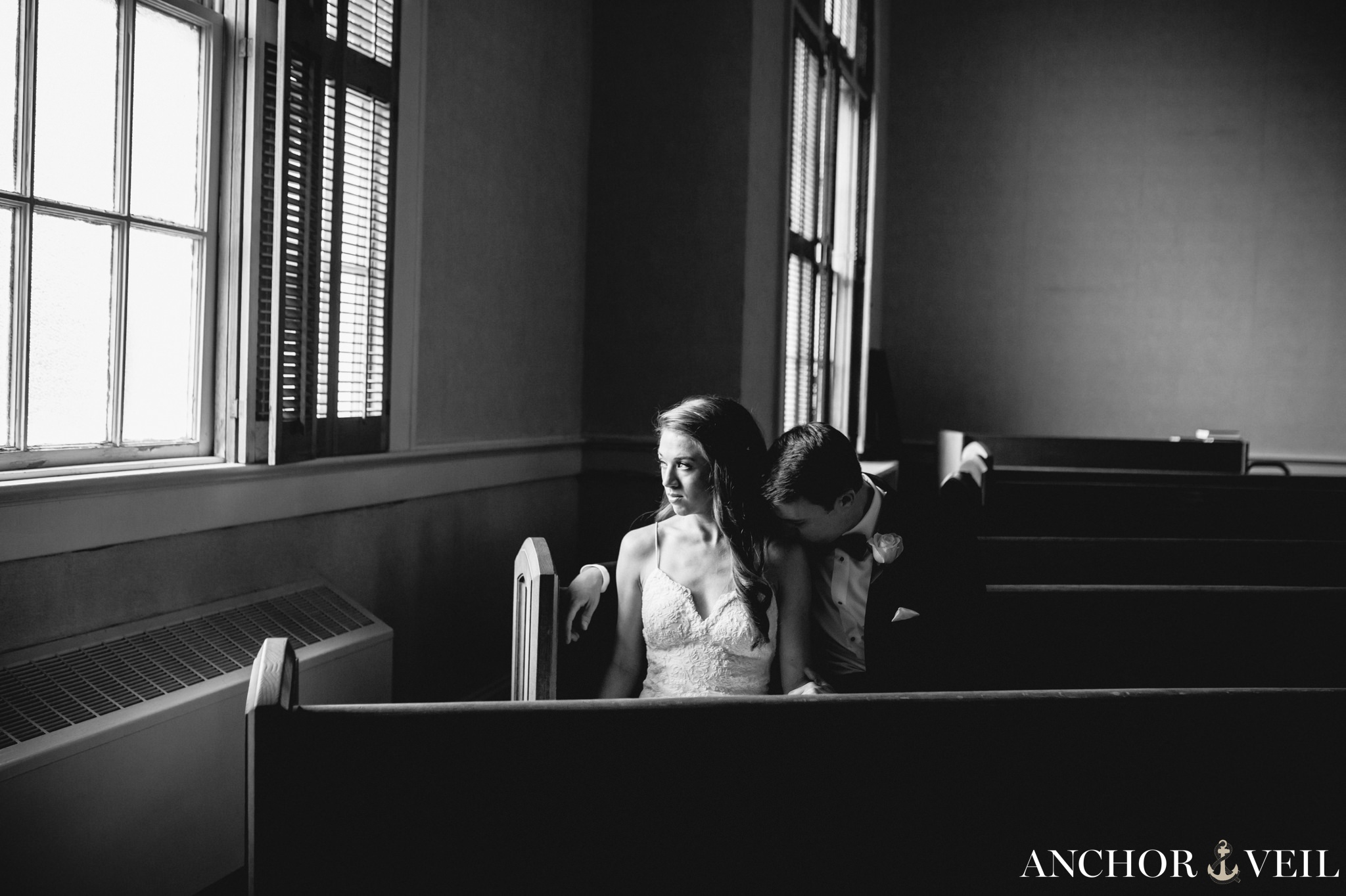 groom kissing brides shoulder next to the window in the church