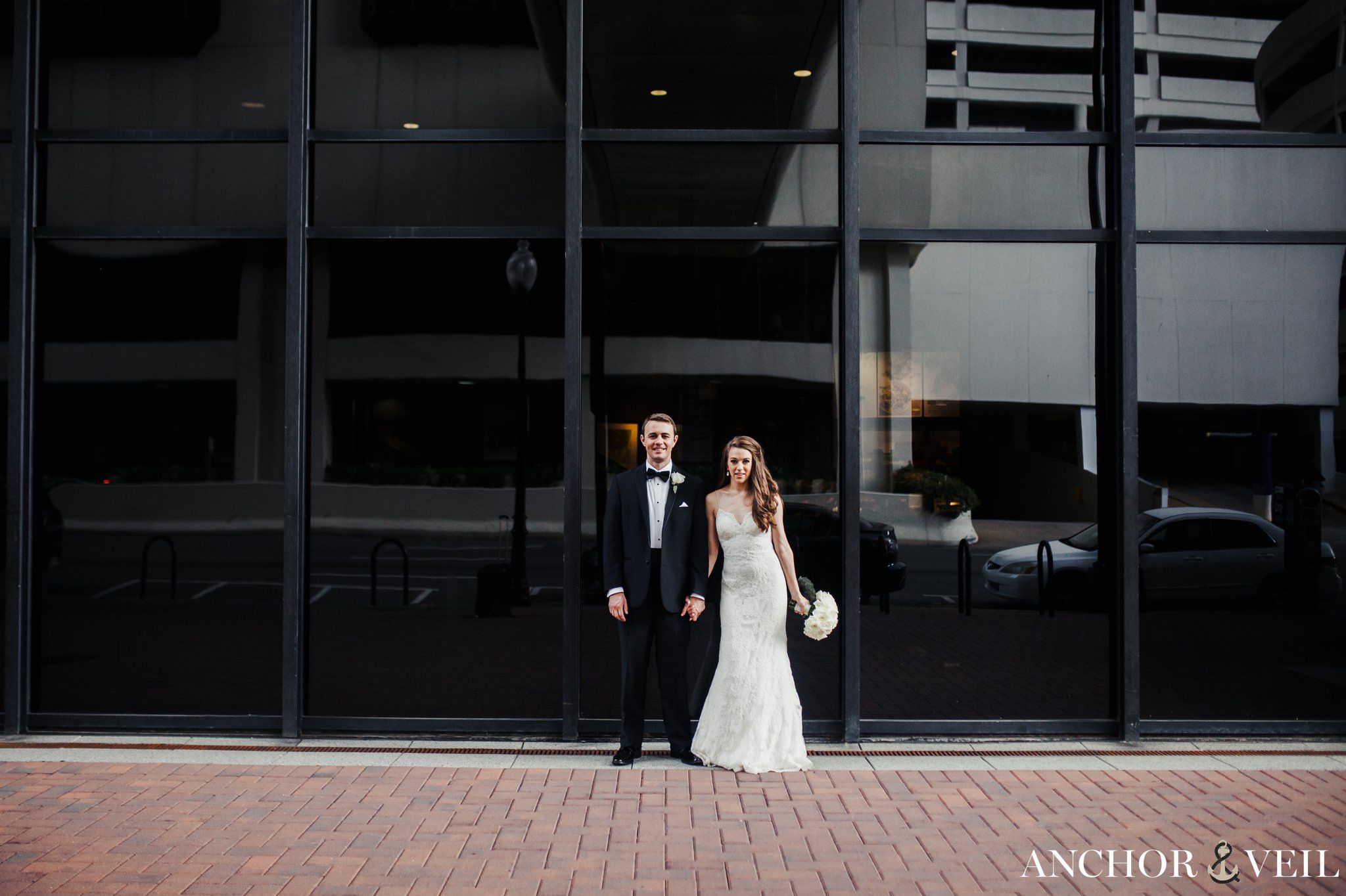 bride and groom hand in hand in front of the dark windows