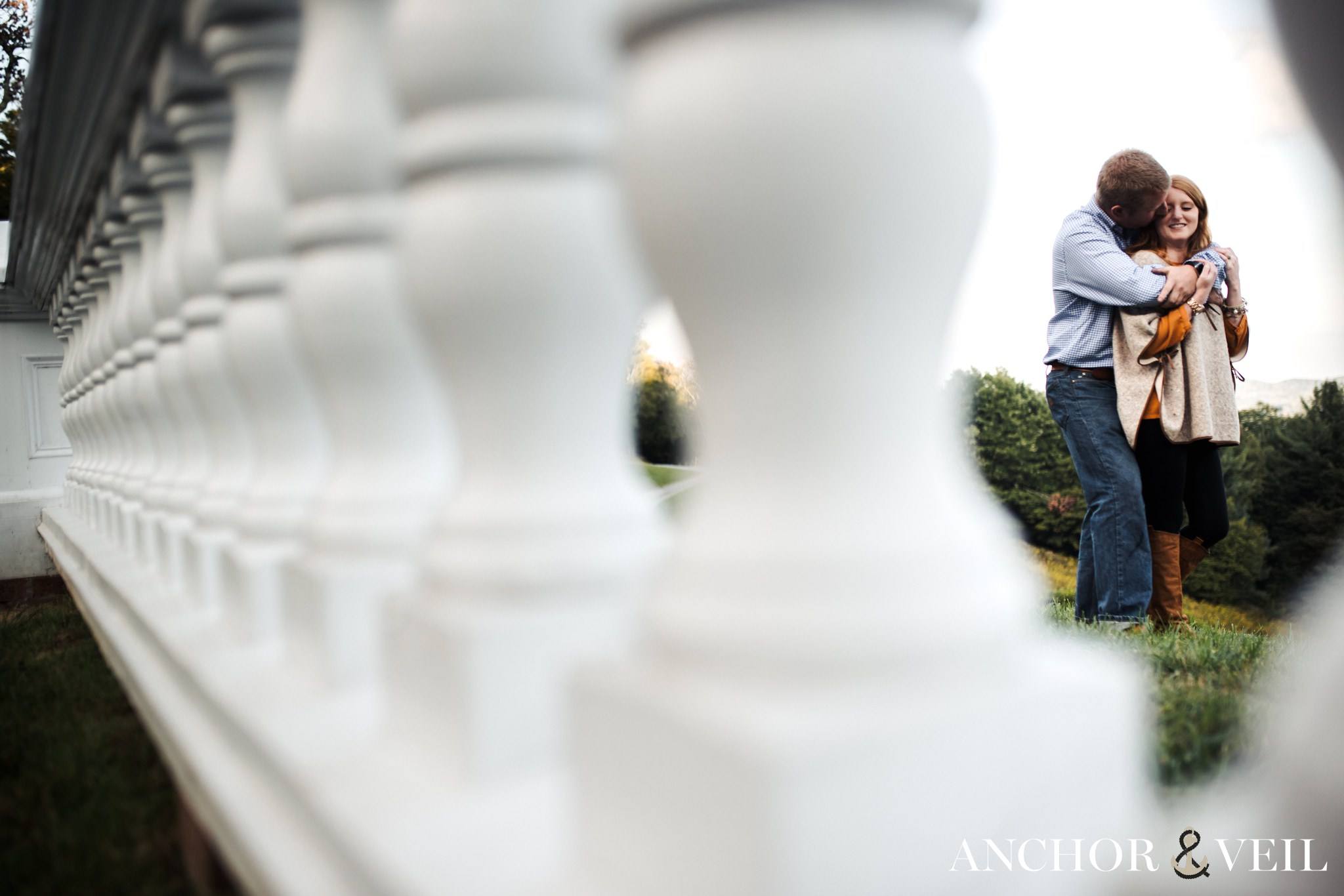 A tender Lovers embrace photographed through the rails of the Moses Cove Manor in Boone for their engagement session