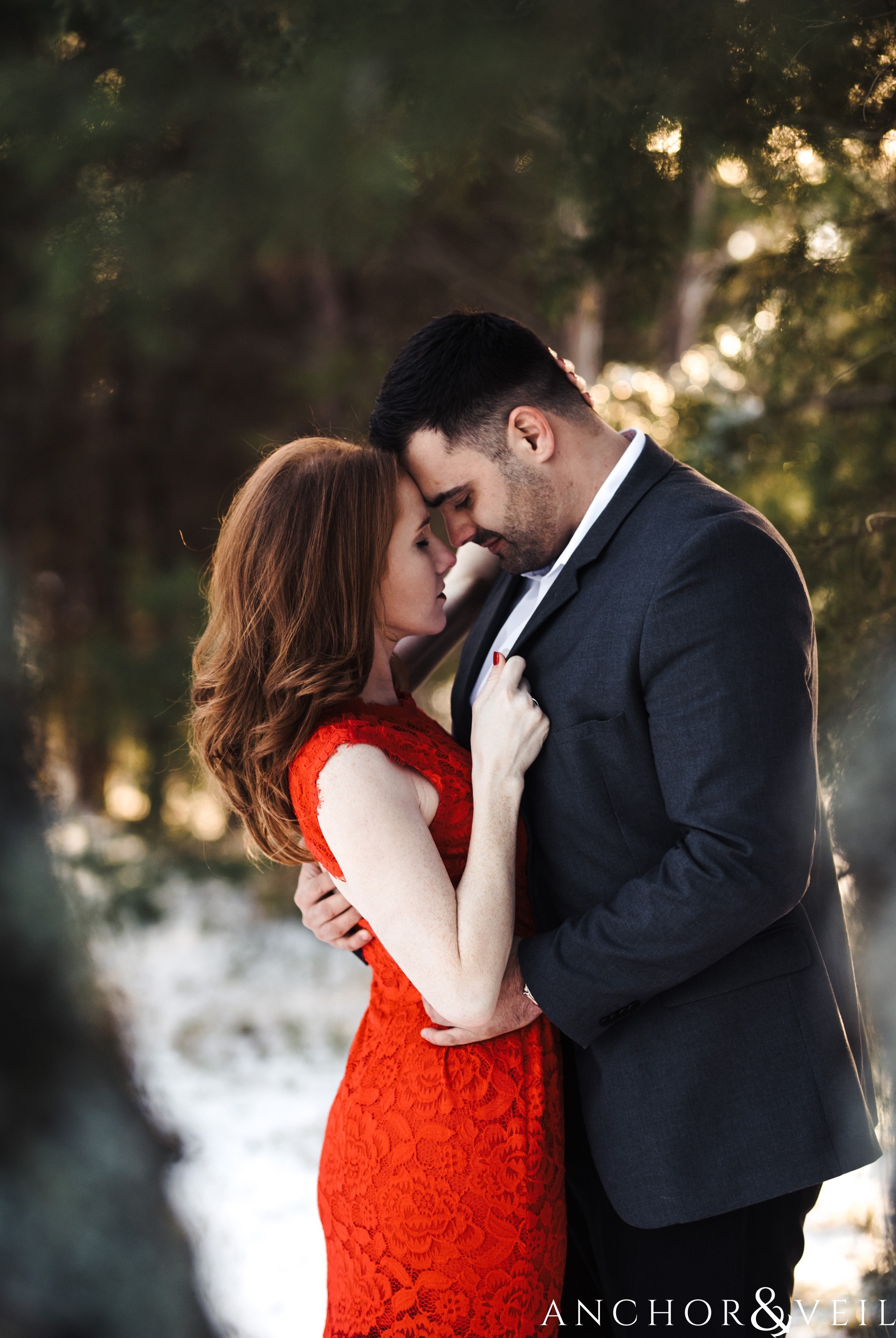 bringing him close by the lapel during their Charlotte Snow engagement session in the woods