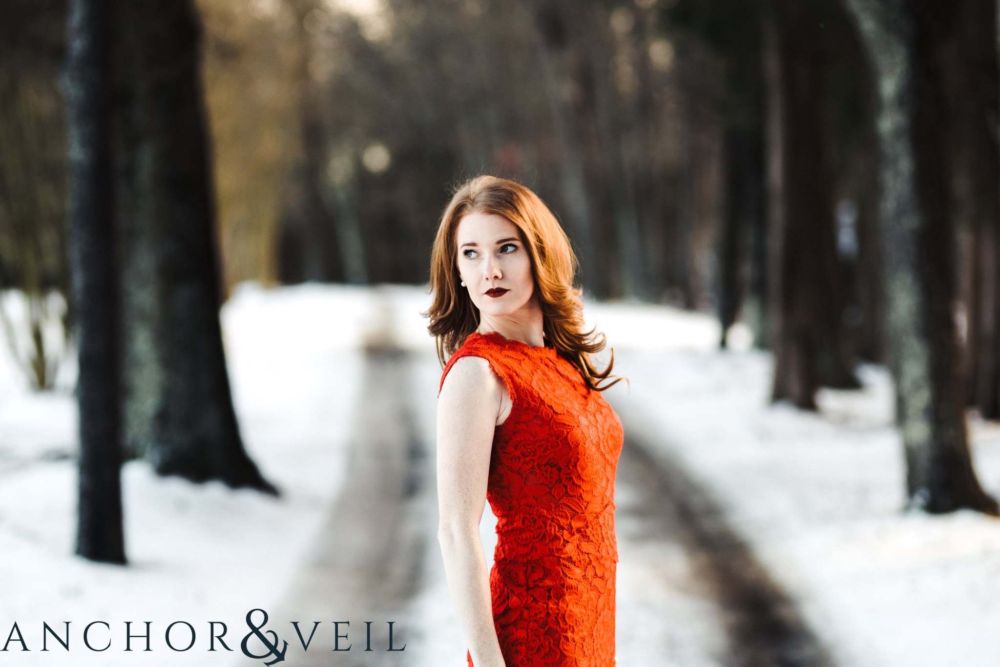 in her red dress looking off during their Charlotte Snow engagement session in the woods