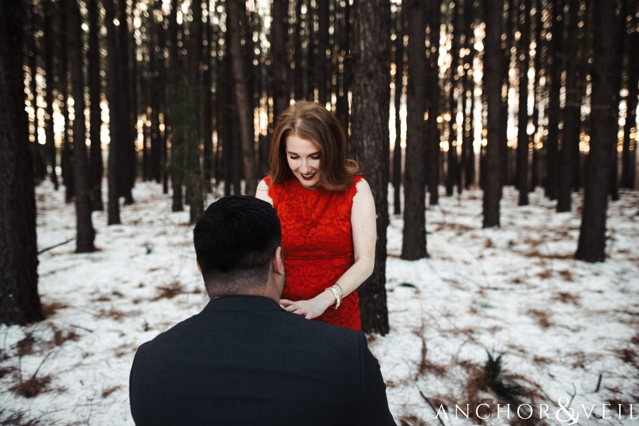 on his knee during their Charlotte Snow engagement session in the woods