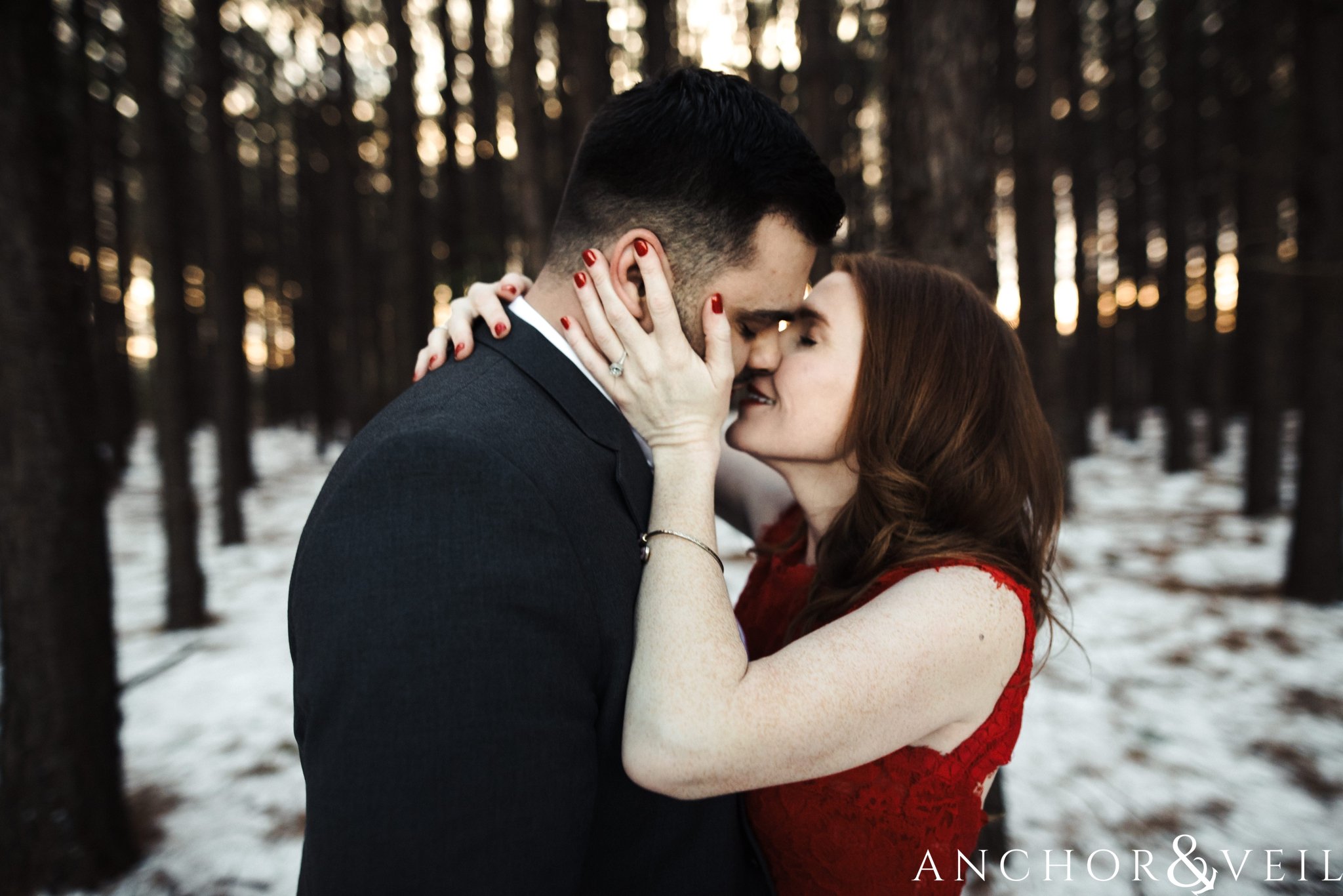 bringing him close for a kiss during their Charlotte Snow engagement session in the woods