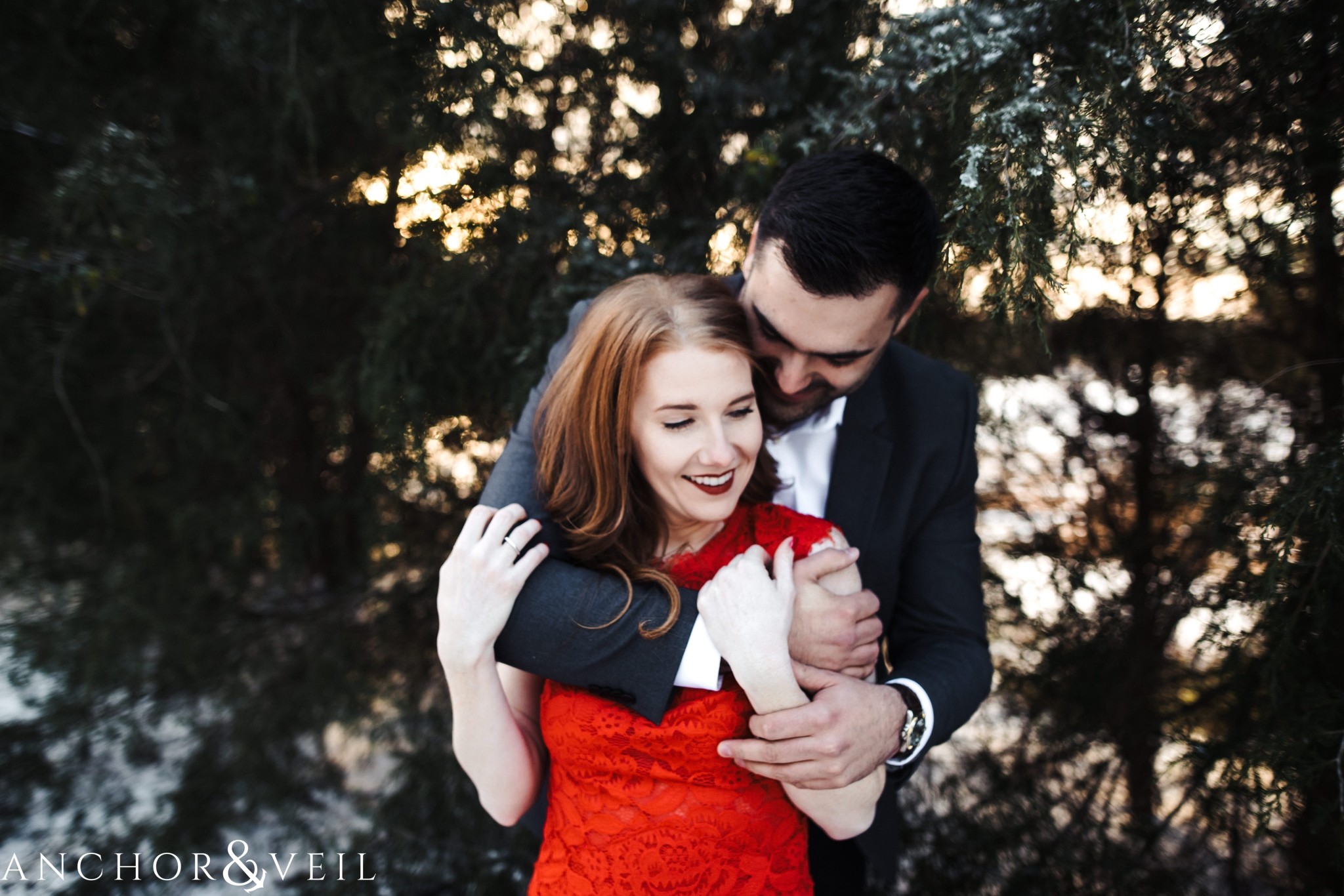 holding her from behind during their Charlotte Snow engagement session in the woods