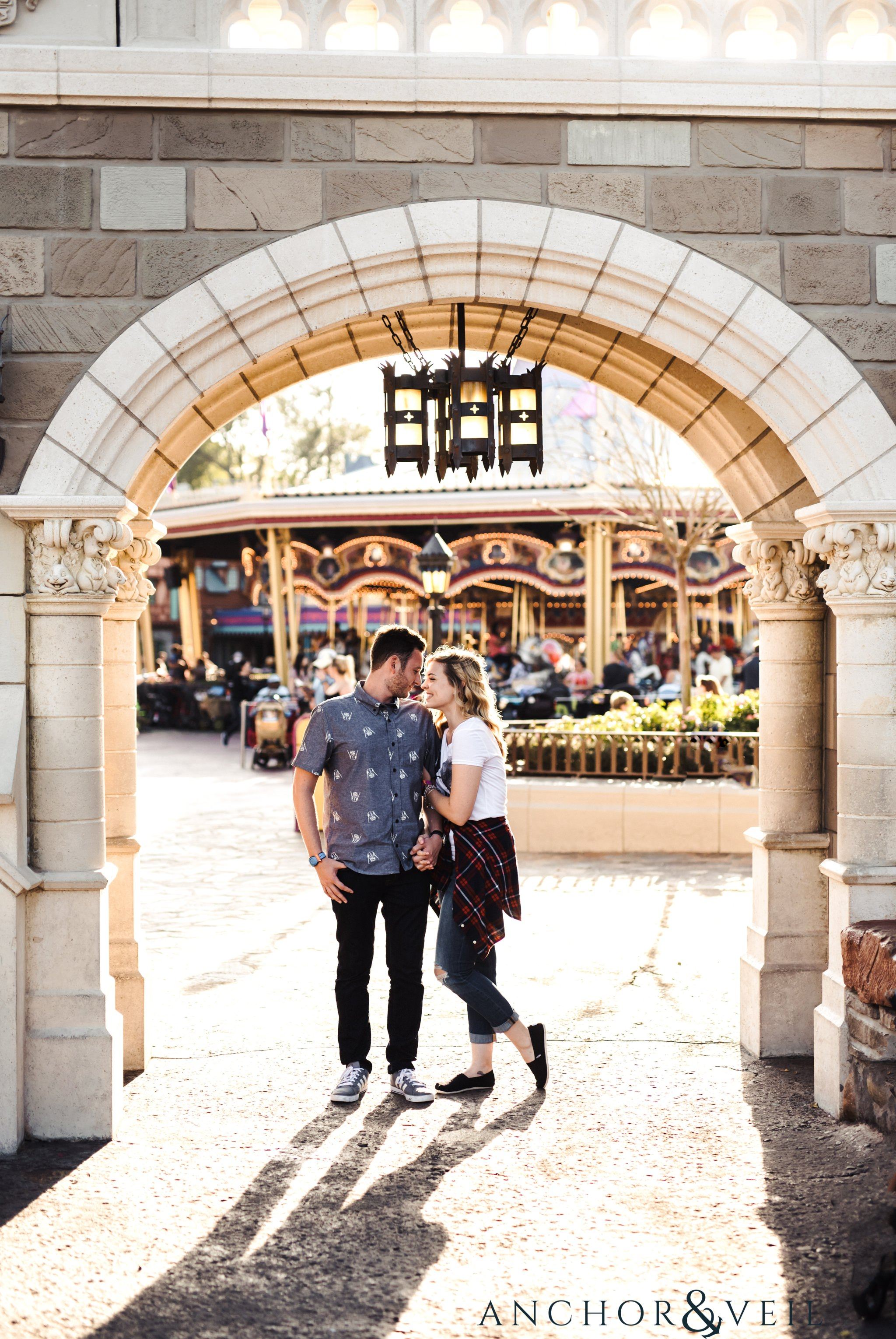 under the arches looking at each other during their Disney world engagement session at Disney's Magic Kingdom