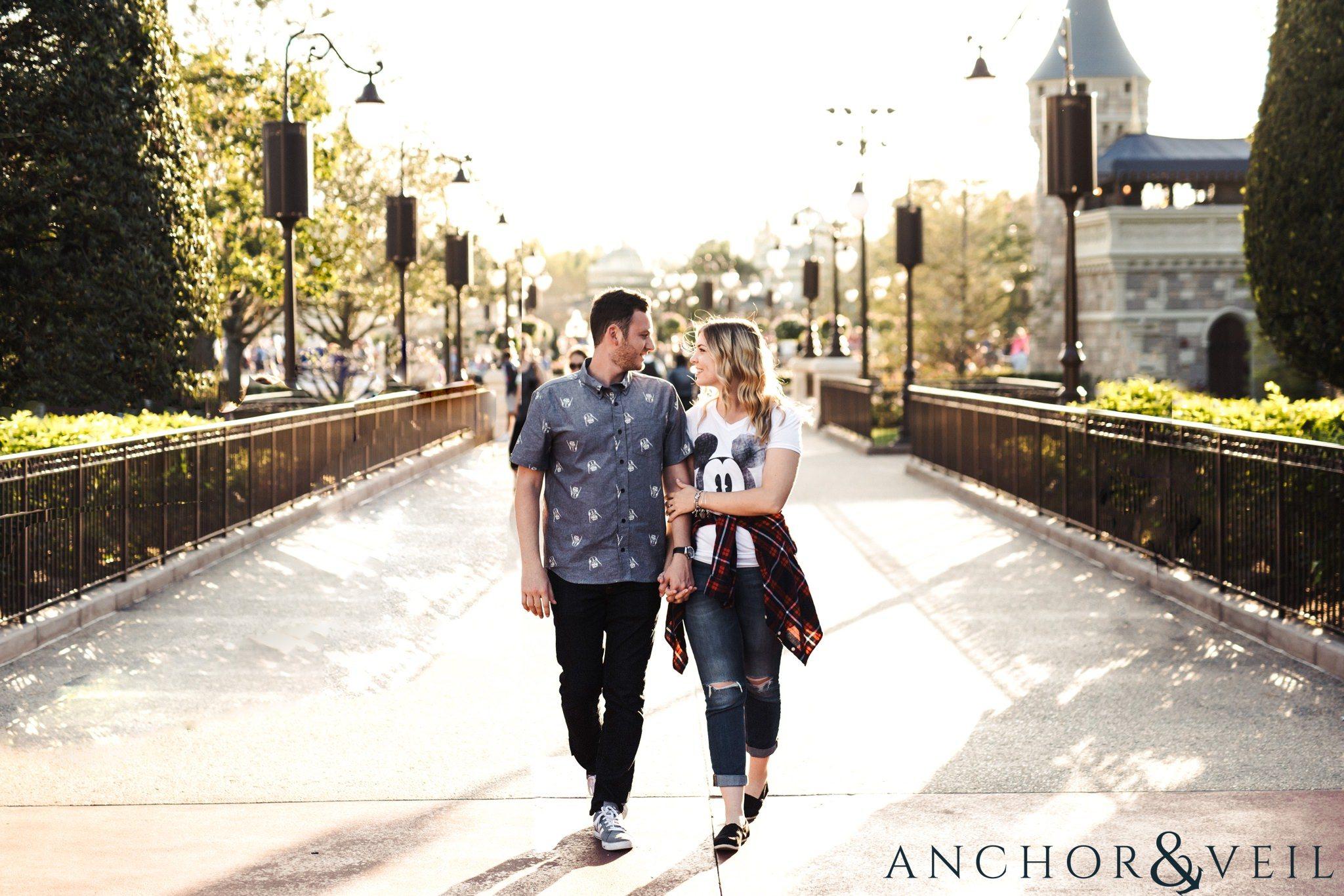 walking hand in hand on the bridge during their Disney world engagement session at Disney's Magic Kingdom