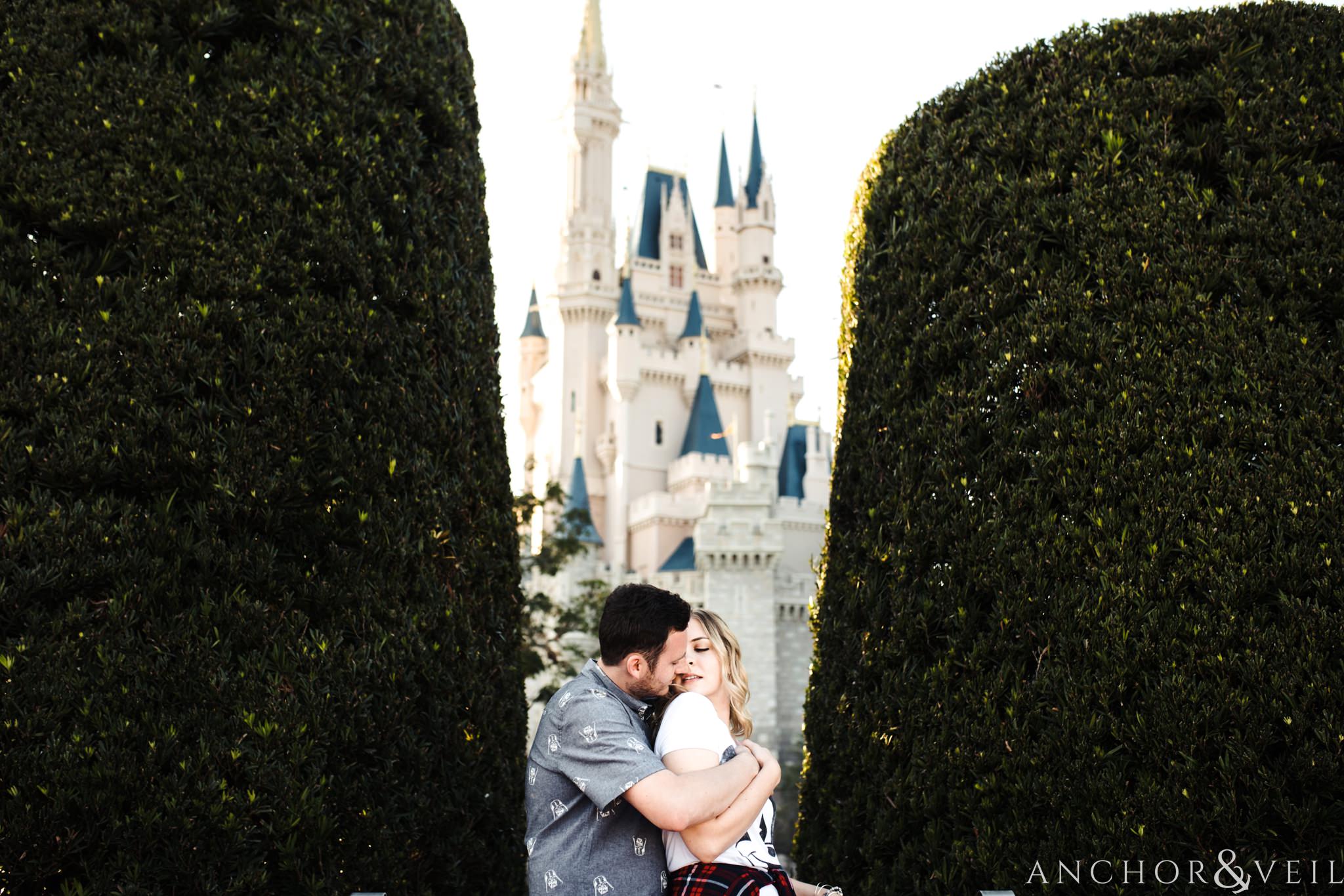kissing in between the trees with the castle in the back during their Disney world engagement session at Disney's Magic Kingdom