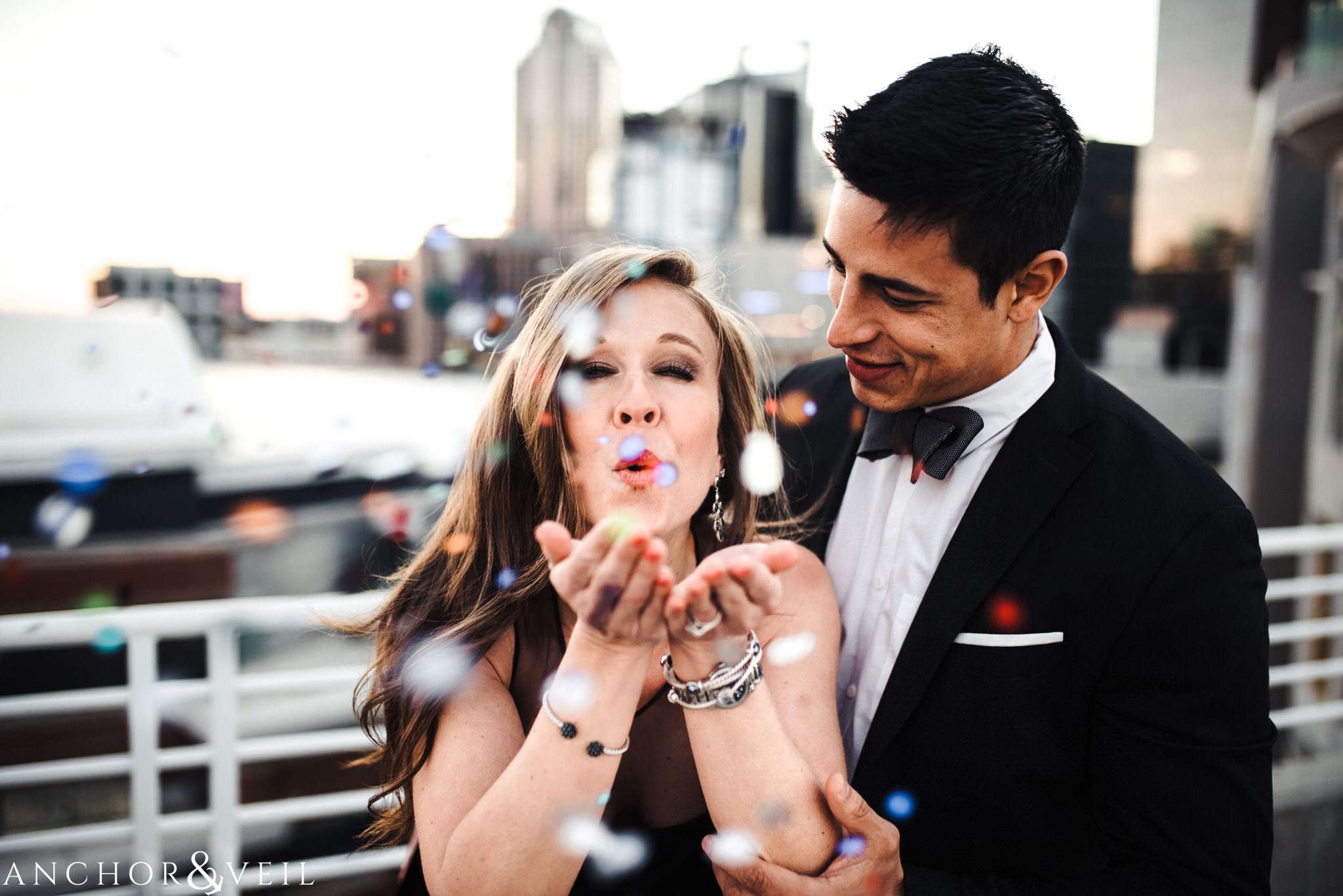 blowing confetti During their Uptown Charlotte Engagement Session