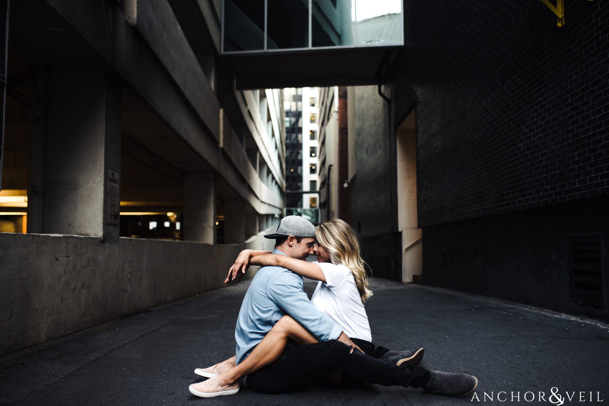 sitting on the ground in the alley with her hands around him uptown Charlotte engagement session