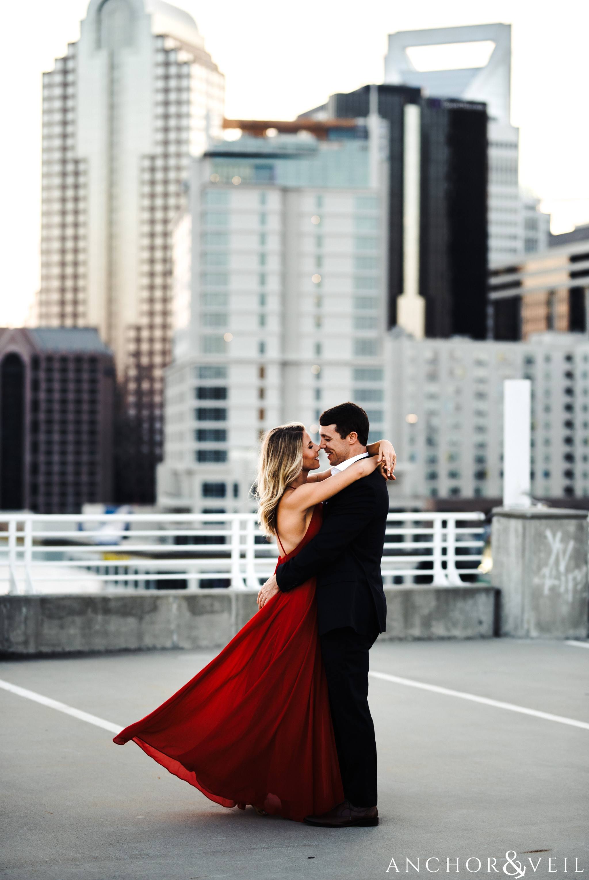 bringing her close in her red dress and his suit with the skyline uptown Charlotte engagement session