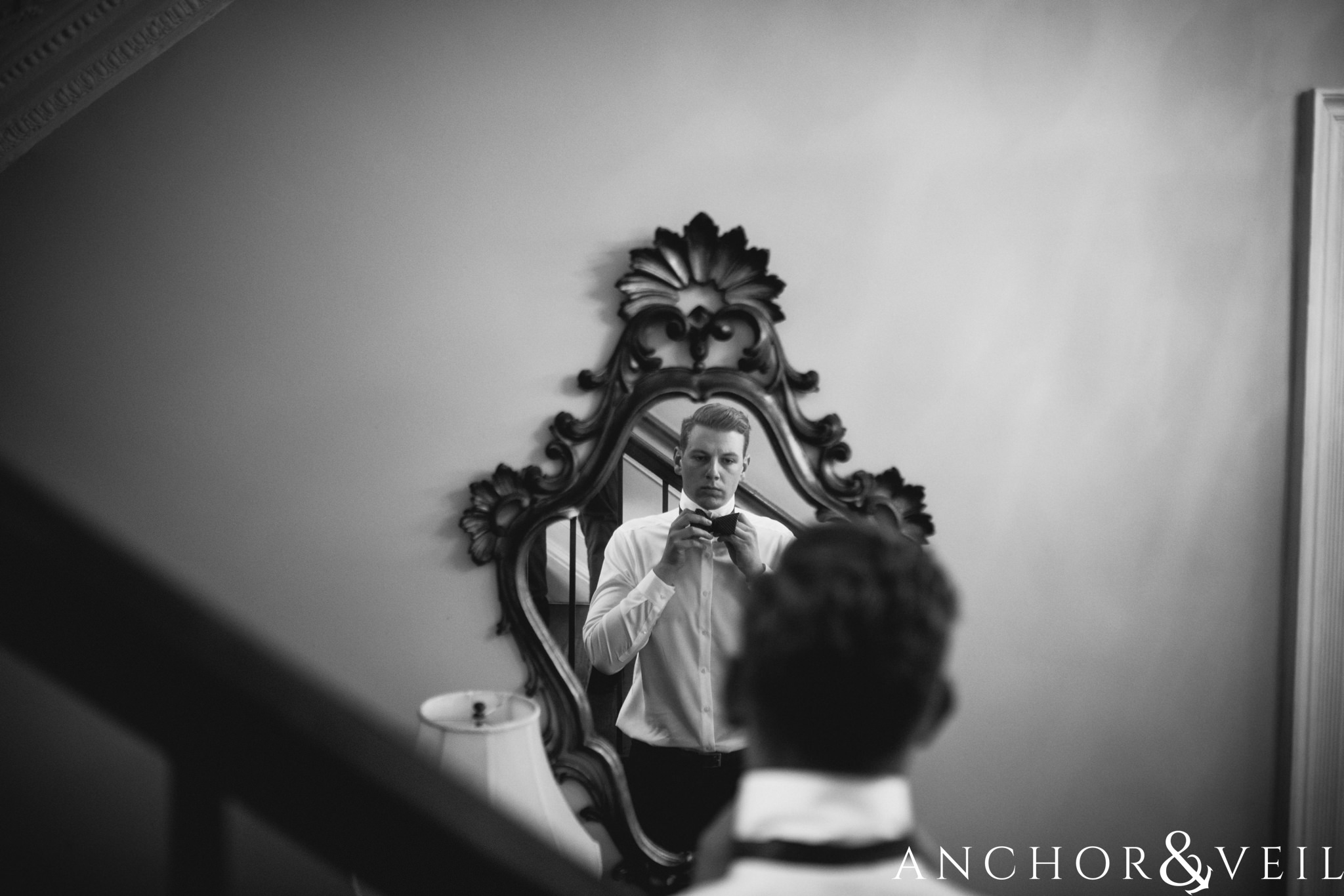 groom in the mirror fixing tie during their William Aiken house Wedding in Charleston Sc
