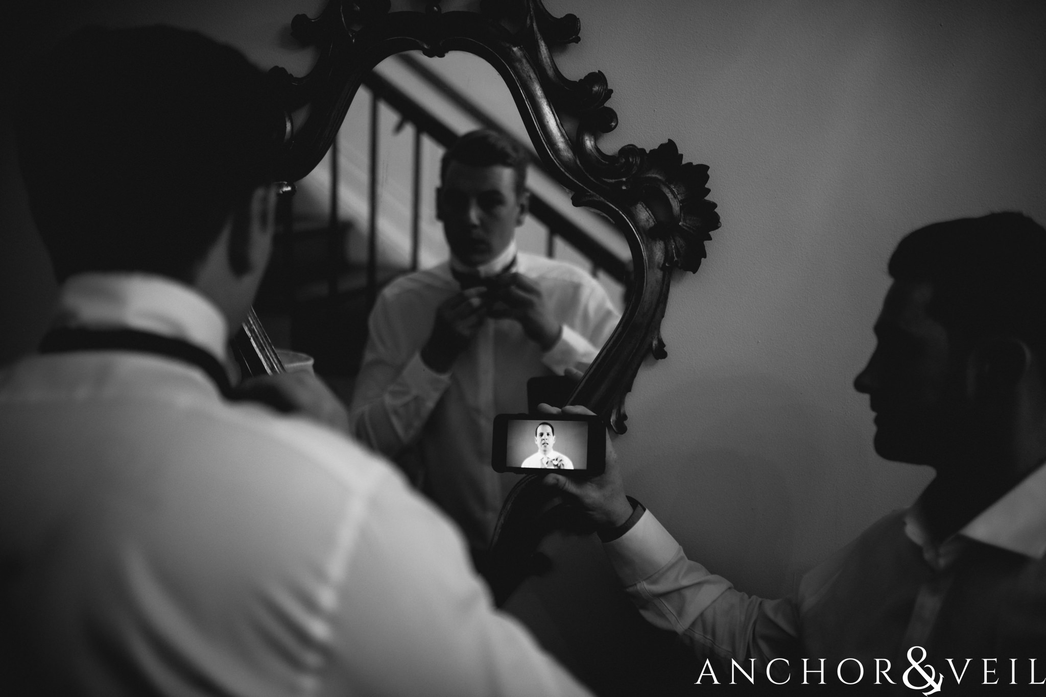 groom learning to tie buy tie during their William Aiken house Wedding in Charleston Sc