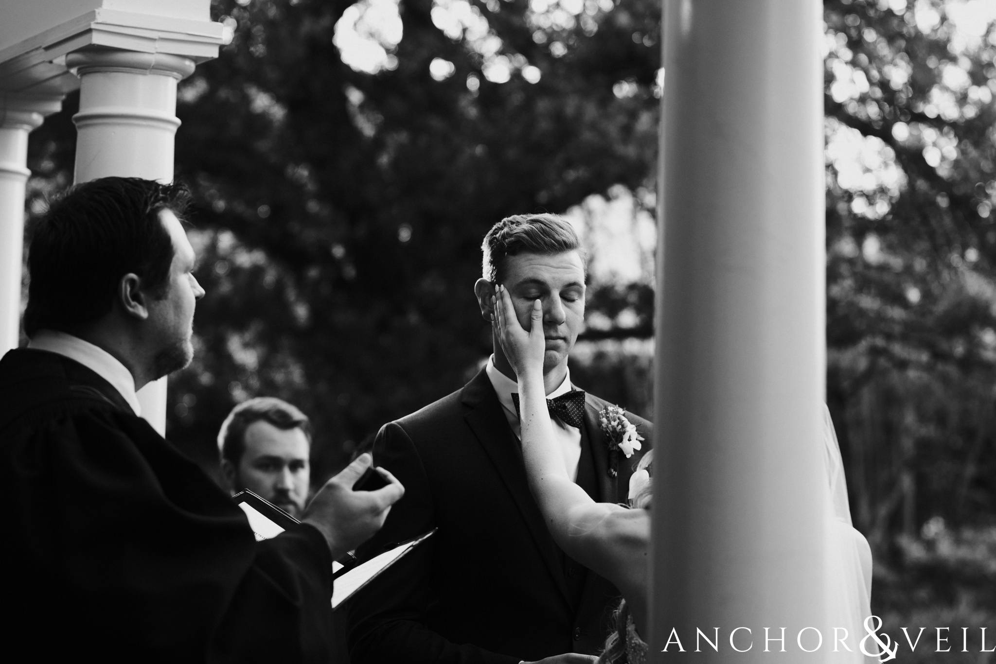 her wiping his tears during the ceremony during their William Aiken house Wedding in Charleston Sc