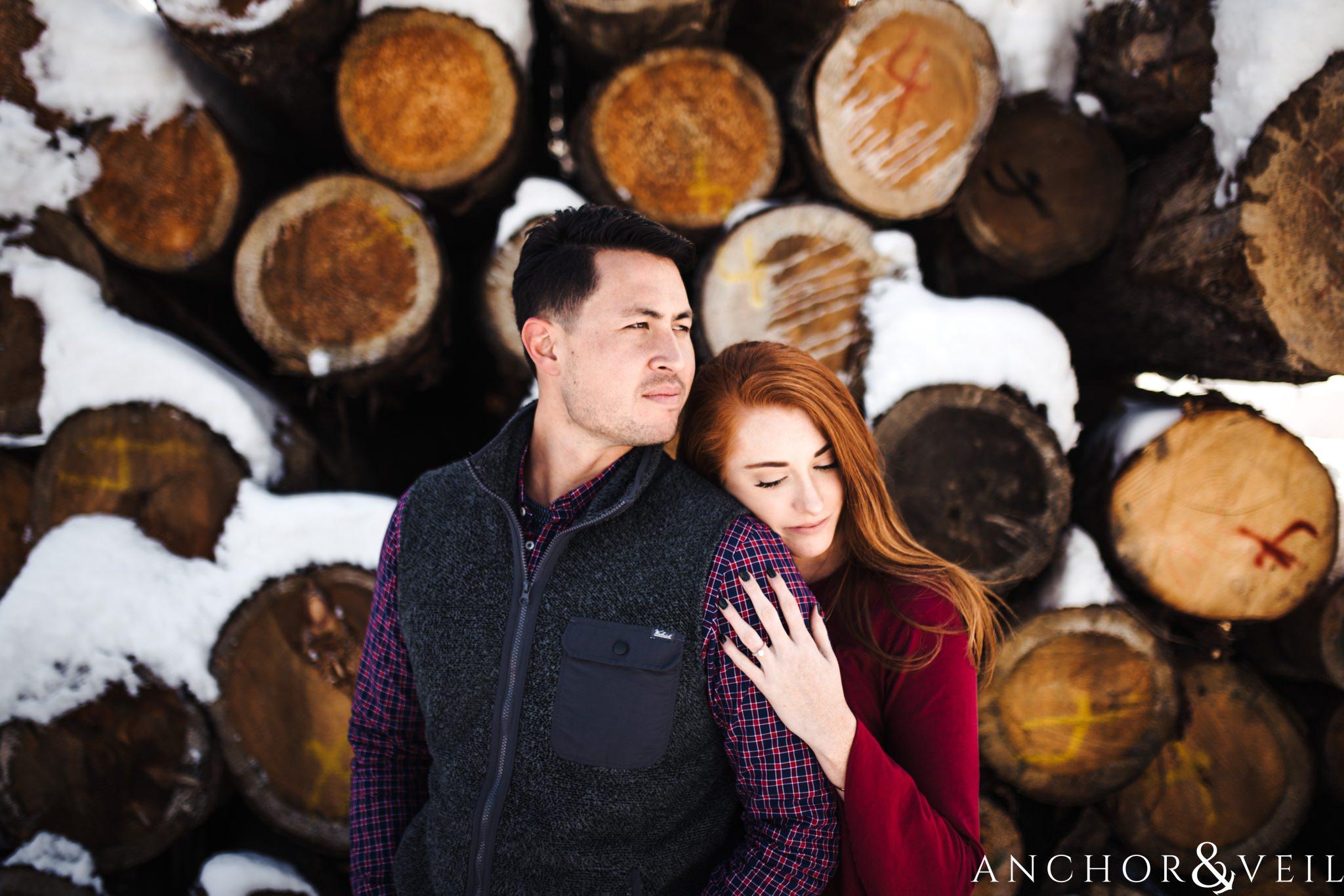 leaning on his shoulder in front of the logs during their Snowy Asheville Engagement Session