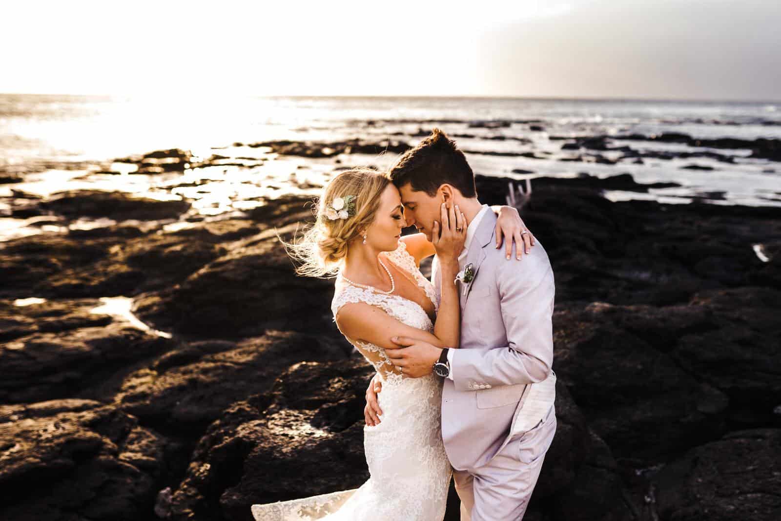 Standing on the rocks holding each other in Hawaii for their destination wedding