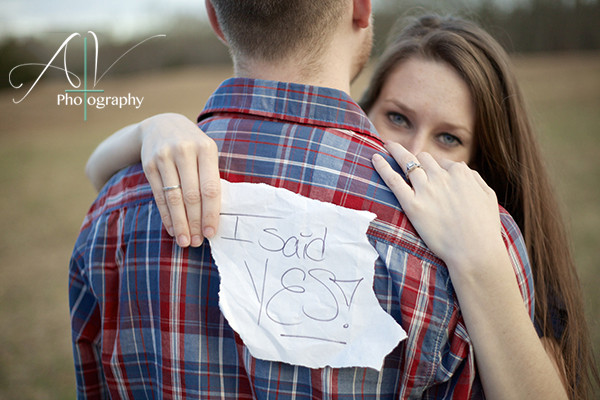 A picture of a couple embracing where she holds a sign saying "I SAID YES!" during their Downtown Concord Engagement Session