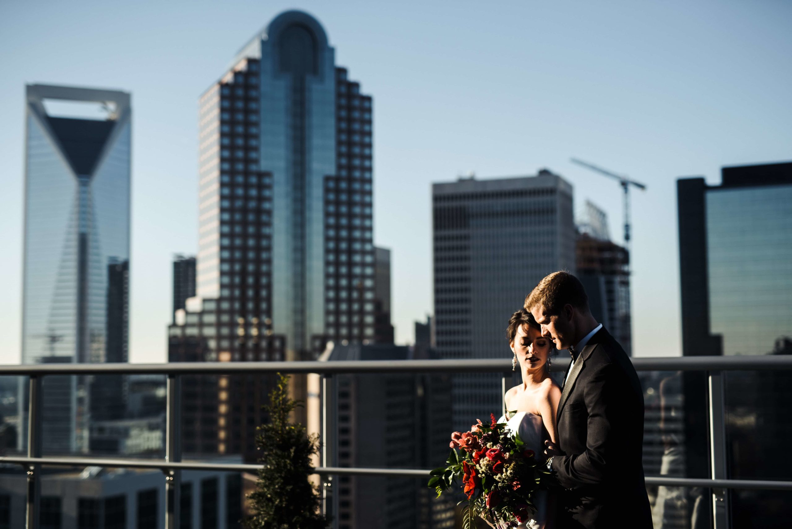 Photograph of Bride & Groom holding each other at sunset with a view of Charlotte NC Skyline in the background